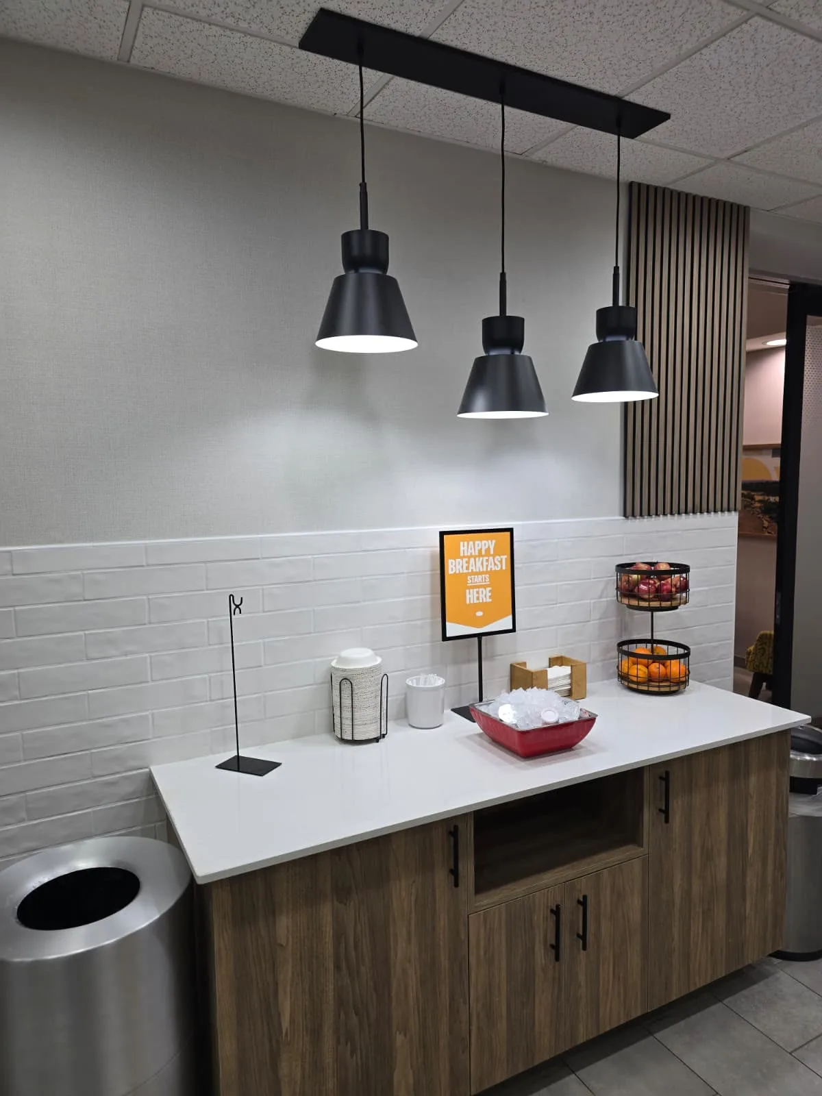 Breakfast serving cabinet with a light countertop beneath three black pendant lights.